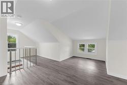 Spacious loft area featuring wood-finish flooring, abundant natural light from multiple windows, a modern metal railing, sloped ceilings, and recessed lighting - 
