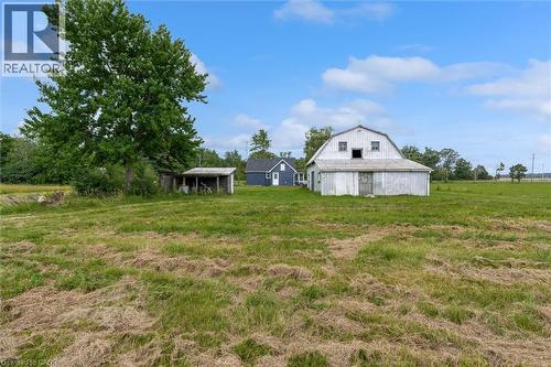 Expansive green field featuring a large gambrel-roof barn, a smaller blue structure, an open-sided shed, and mature trees - 87 Mud Street E, Grimsby, ON 