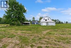 Expansive green field featuring a large gambrel-roof barn, a smaller blue structure, an open-sided shed, and mature trees - 