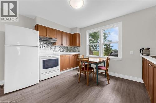 Kitchen featuring wood-finish flooring, wood cabinetry, white appliances, a mosaic tile backsplash, and a double window - 87 Mud Street E, Grimsby, ON 