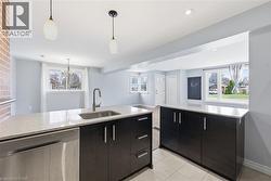 Kitchen with stainless steel dishwasher, a peninsula, light stone counters, decorative light fixtures, and dark cabinets - 