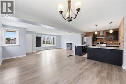 Kitchen featuring open floor plan, brick wall, light wood-type flooring, stainless steel electric stove, and suspended lighting - 