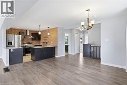 Kitchen featuring brick wall, stainless steel appliances, light wood-style flooring, hanging lights, and light stone counters - 