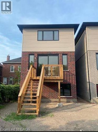 Rear exterior featuring a red brick facade with light beige horizontal siding, a wooden deck with railing, and exterior staircase - 48 Melbourne Street, Hamilton, ON - Outdoor