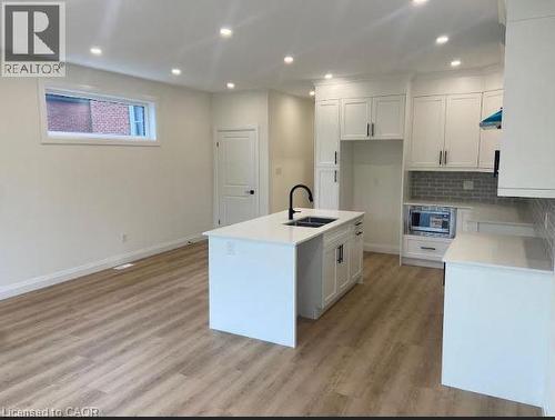 Open-concept kitchen with a central island featuring a double sink and matte black faucet, surrounded by white cabinetry with black hardware - 48 Melbourne Street, Hamilton, ON - Indoor Photo Showing Kitchen With Double Sink