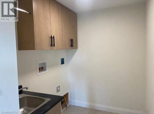 Utility room featuring a stainless steel sink, dark countertop, and light wood-finish cabinetry with black hardware - 48 Melbourne Street, Hamilton, ON - Indoor