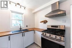 Kitchen featuring butcher block countertops, white cabinetry with black hardware, and a stainless steel gas range with coordinating vent hood - 