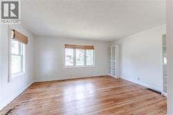Spacious living room featuring original hardwood flooring, multiple windows with blinds, and white glass cabinets - 