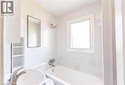 Bathroom featuring a ceramic tile bath surround, chrome shower fixtures, a window, and an integrated white bathtub - 