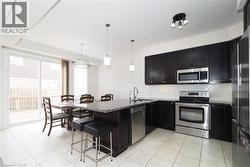 Kitchen featuring dark wood-finish cabinetry, stainless steel appliances, a granite-finish island with seating, a white subway tile backsplash, and ceramic tile flooring - 