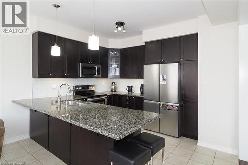 Kitchen featuring a large island with a granite countertop, stainless steel appliances, dark wood cabinetry, and a subway tile backsplash - 213 Seabrook Drive, Kitchener, ON 