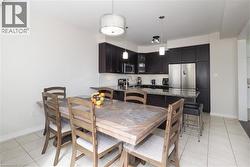 Open-concept kitchen and dining area featuring dark wood-finish cabinetry, stainless steel appliances, a granite countertop island, and ceramic tile flooring - 