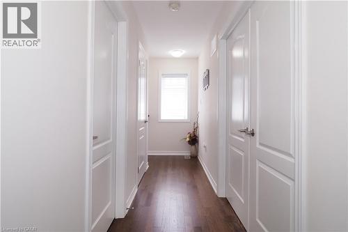 Hallway featuring dark wood-finish flooring, white paneled doors with brushed nickel hardware, and a window with horizontal blinds - 213 Seabrook Drive, Kitchener, ON 