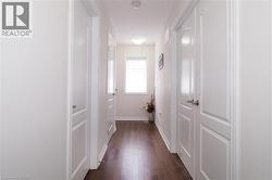 Hallway featuring dark wood-finish flooring, white paneled doors with brushed nickel hardware, and a window with horizontal blinds - 