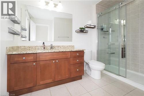 Bathroom featuring a spacious wood-finish vanity with a light-colored granite-style countertop, undermount sink, and a large mirror - 213 Seabrook Drive, Kitchener, ON 