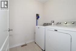 Laundry area featuring neutral wall paint, tile flooring, and a white interior door with brushed nickel hardware - 