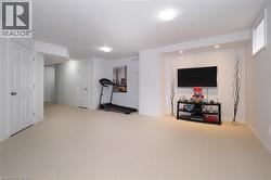 Spacious lower-level room featuring light-colored carpeting, white baseboards, and white painted walls - 