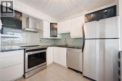 Contemporary kitchen featuring white cabinetry, dark countertops, stainless steel appliances, a glass tile backsplash, and light wood-finish flooring - 