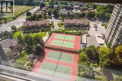Multiple tennis courts with red surfacing and green playing areas, surrounded by mature trees - 