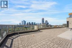 Rooftop patio with paver flooring, modern glass railings, and a prominent cityscape - 