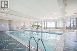 Indoor swimming pool with integrated spa, surrounded by floor-to-ceiling windows, white tiled flooring, and an adjacent fitness area - 