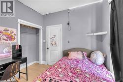 Room with light gray walls, wood-finish flooring, a white interior door, an open closet, and a white wall-mounted shelf - 