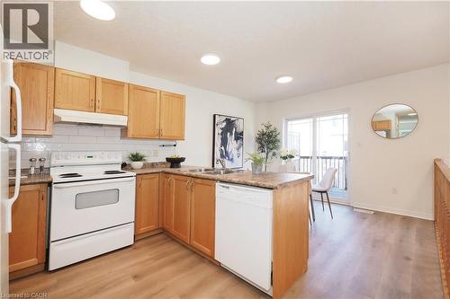 Kitchen featuring wood cabinetry, white subway tile backsplash, white appliances, and wood-finish flooring - 619 Wild Ginger Avenue Unit# H47, Waterloo, ON - Indoor Photo Showing Kitchen With Double Sink