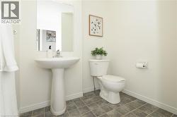 Pedestal sink with chrome faucet, square wall mirror, white toilet, tiled flooring, and white baseboards - 