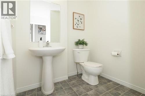 Pedestal sink with chrome faucet, square wall mirror, white toilet, tiled flooring, and white baseboards - 619 Wild Ginger Avenue Unit# H47, Waterloo, ON - Indoor Photo Showing Bathroom