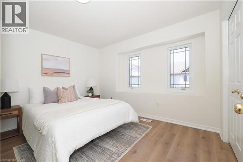 White-painted room featuring wood-finish flooring and two windows with decorative grilles - 619 Wild Ginger Avenue Unit# H47, Waterloo, ON - Indoor Photo Showing Bedroom