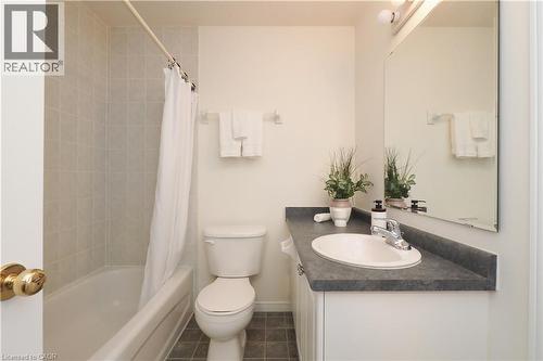 Bathroom featuring a bathtub with tiled surround, a white toilet, a vanity with a dark countertop and integrated sink, and a large wall-mounted mirror - 619 Wild Ginger Avenue Unit# H47, Waterloo, ON - Indoor Photo Showing Bathroom