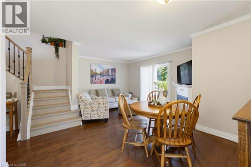 Interior featuring wood-finish flooring throughout, a staircase with wood newel posts and black iron balusters, a built-in fireplace with a white mantel, and crown molding - 520 Mayflower Street, Waterloo, ON - Indoor Photo Showing Dining Room