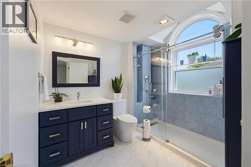 Bathroom featuring a floating vanity with a white countertop and blue cabinetry, a glass-enclosed shower with blue mosaic tile, a commode, and an arched window - 520 Mayflower Street, Waterloo, ON - Indoor Photo Showing Bathroom