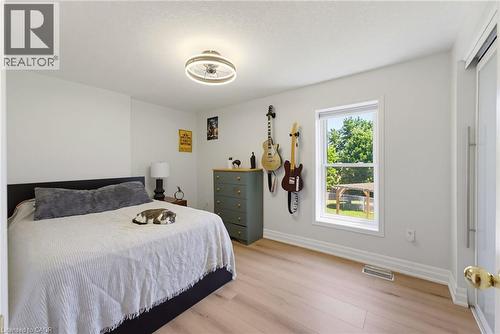 Bright interior space featuring wood-finish flooring, a contemporary ceiling light fixture, a large window with white trim, and a white interior door - 520 Mayflower Street, Waterloo, ON - Indoor Photo Showing Bedroom