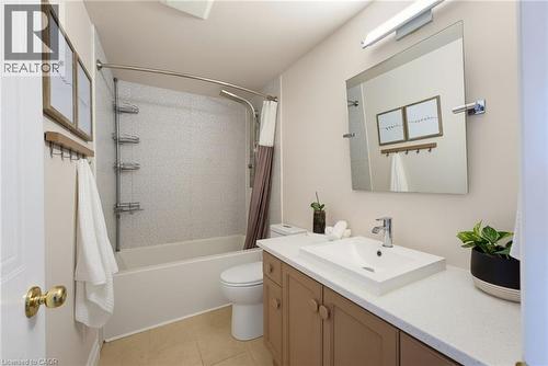 Bathroom featuring a built-in tub with tile surround, a low-profile toilet, a vanity with a white countertop, an integrated rectangular sink, and a wall-mounted mirror with overhead lighting - 520 Mayflower Street, Waterloo, ON - Indoor Photo Showing Bathroom