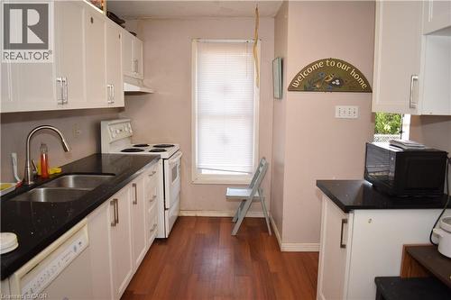 Kitchen featuring white cabinetry, black speckled countertops, a double basin stainless steel sink with a gooseneck faucet, a white oven, and wood-finish flooring - 249 Cedarbrae Avenue Unit# 1, Waterloo, ON 