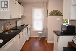 Kitchen featuring white cabinetry, black speckled countertops, a double basin stainless steel sink with a gooseneck faucet, a white oven, and wood-finish flooring - 