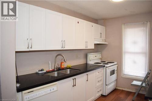 Kitchen featuring white cabinetry, dark countertops, a double basin stainless steel sink with a gooseneck faucet, a white range, and wood-finish flooring - 249 Cedarbrae Avenue Unit# 1, Waterloo, ON 