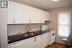 Kitchen featuring white cabinetry, dark countertops, a double basin stainless steel sink with a gooseneck faucet, a white range, and wood-finish flooring - 