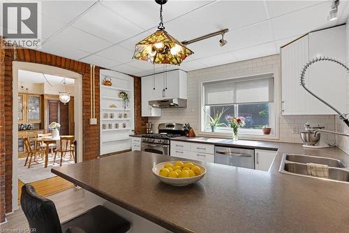 Kitchen featuring a large central island with seating, stainless steel appliances, white cabinetry, a subway tile backsplash, and exposed brick accents - 630 Lawrence Street, Cambridge, ON - Indoor Photo Showing Kitchen With Double Sink With Upgraded Kitchen