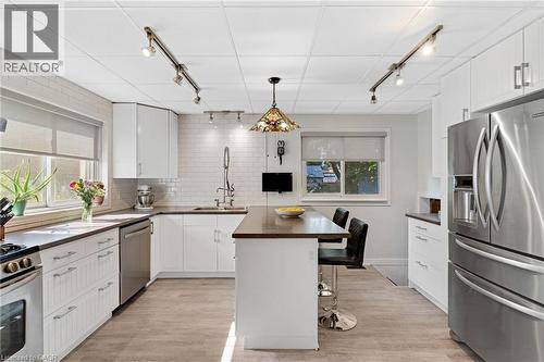 Modern kitchen featuring white cabinetry, a central island with countertop seating, stainless steel appliances, and wood-finish flooring - 630 Lawrence Street, Cambridge, ON - Indoor Photo Showing Kitchen With Double Sink With Upgraded Kitchen
