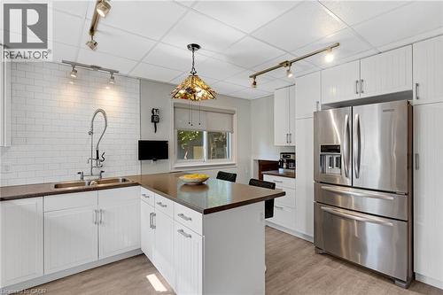 White cabinetry and a dark countertop define this kitchen, featuring a stainless steel refrigerator, white subway tile backsplash, and a double basin sink with a high-arc faucet - 630 Lawrence Street, Cambridge, ON - Indoor Photo Showing Kitchen With Double Sink