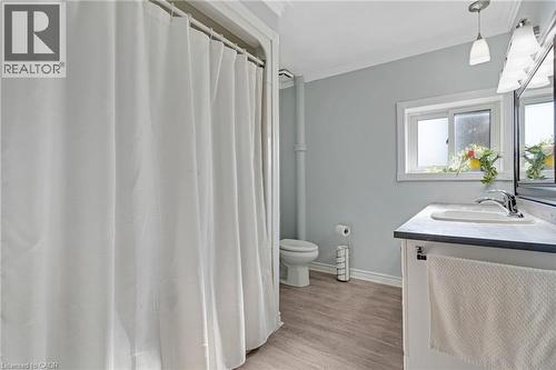 Bathroom featuring a shower with a white curtain, light wood-finish flooring, a white vanity with a dark countertop, an integrated sink with a chrome faucet, and a wall-mounted mirror - 630 Lawrence Street, Cambridge, ON - Indoor Photo Showing Bathroom