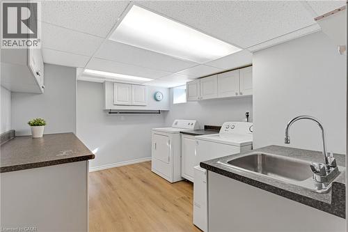 Laundry room featuring wood-finish flooring, white cabinetry, dark countertops, and a utility sink with a chrome faucet - 630 Lawrence Street, Cambridge, ON - Indoor Photo Showing Laundry Room