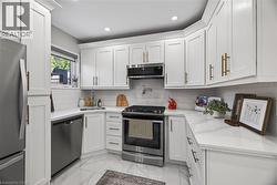 Kitchen featuring white shaker-style cabinetry with gold-toned hardware, stainless steel appliances, white subway tile backsplash, recessed lighting, and white stone countertops - 