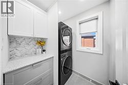 Laundry room with stacked washing machine and dryer, light tile patterned floors, cabinet space, and recessed lighting - 