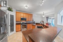 Kitchen featuring wood-finish cabinetry, stainless steel appliances, speckled countertops, and tile flooring - 