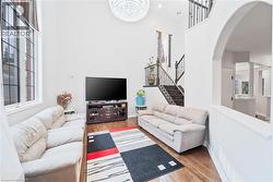 Double-height living space featuring large windows, wood-finish flooring, and a contemporary chandelier - 