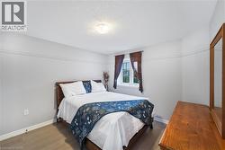 Bedroom featuring light wood-finish flooring, white baseboards, and a single window with dark brown curtain panels - 