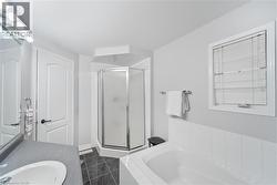 Bathroom featuring a corner shower enclosure with frosted glass, a built-in bathtub with white tile surround, a vanity with a white basin and gray countertop, dark tiled flooring, and a window with bl - 